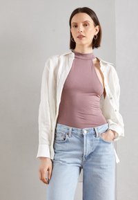Obtažený bezrukávový mauve body pod volnou bílou lněnou košilí, v kombinaci se světlými modrými džínami s vysokým pasem. Jednoduché kruhové náušnice.
