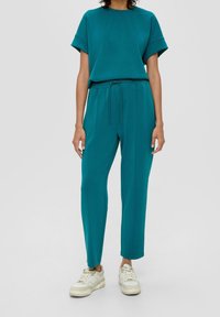 Teala katoenmix korte mouw top gecombineerd met bijpassende joggers met een verstelbare taille. Model draagt witte sneakers.