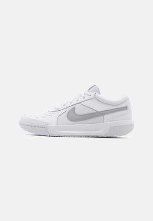 Baskets basses blanches avec le swoosh Nike gris clair, lacets, bout perforé et semelle texturée, vues de profil sur un fond gris.