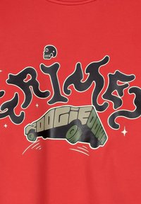 Rode t-shirt met gedurfde, gestileerde zwarte en groene tekst en een afbeelding van een auto. Het ontwerp bevat een schedel en sterren als accenten.