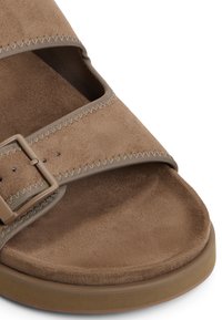 Brown suede sandal with a wide strap, adjustable buckle, and cushioned sole. Features stitched accents and a smooth texture.