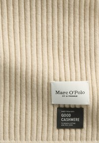 Tissu en cachemire beige avec une texture côtelée verticale. Comprend deux étiquettes : l'une blanche avec "Marc O'Polo" et l'autre noire indiquant "Good Cashmere".