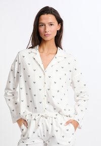 Weißes Pyjama-Set mit teal- und rosa Herzmustern, bestehend aus einem knopfbaren Hemd mit Tasche und lässigen Hosen mit elastischem Bund.