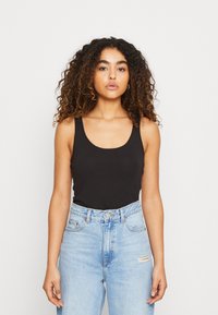 Black sleeveless top made from soft fabric, featuring a rounded neckline and fitted design, paired with light blue high-waisted jeans.