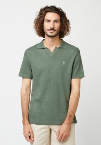 Kurzarm-Polohemd in olivgrün, mit V-Ausschnitt, weichem Stoff und kleinem Baum-Logo auf der linken Brust.