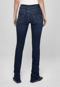 Tmavomodré rozšírené džínsy z denimu s vysokým pásom, dvoma zadnými vreckami a strapatými lemami. Švy sú zdobené zlatým prešívaním.