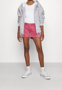 Sweat à capuche gris zippé, débardeur blanc, short en jean rose et baskets montantes blanches avec des accents noirs. Look décontracté et simple de style urbain.