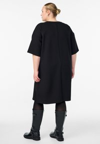 Čierne oversized šaty s krátkymi rukávmi, okrúhlym výstrihom a rovný strih. Skombinované s čiernymi koženými čižmami po kolená so sponami.