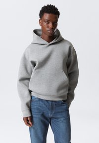 Grijze sweatshirt met capuchon en een kangaroozak aan de voorkant, met een ontspannen pasvorm en geribbelde manchetten, gecombineerd met blauwe denim jeans.