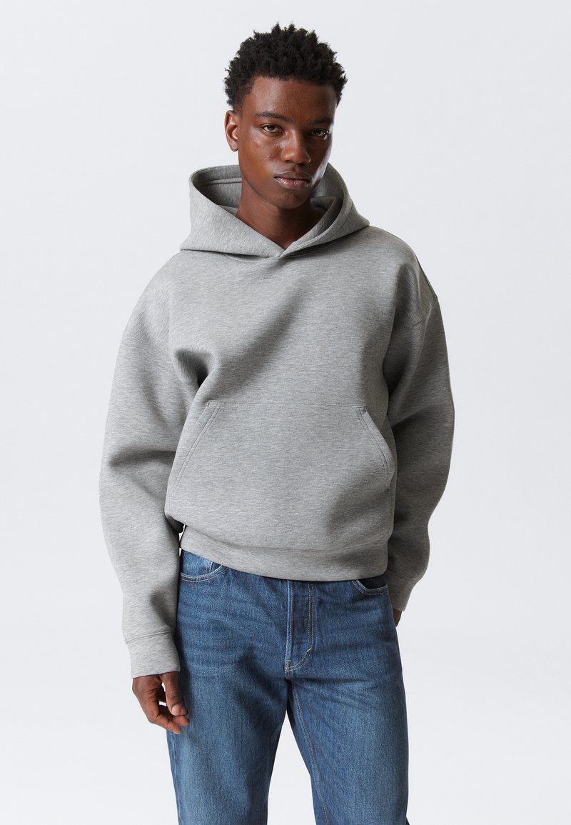 Grijze sweatshirt met capuchon en een kangaroozak aan de voorkant, met een ontspannen pasvorm en geribbelde manchetten, gecombineerd met blauwe denim jeans.