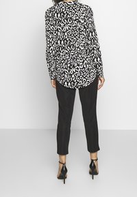Langærmet sort-hvid leopardprint skjorte med rund bund, parret med tætsiddende sorte bukser og sorte højhælede sko.