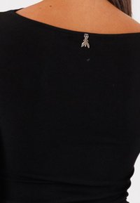 Top nero con un'ampia scollatura a spalle scoperte. Accento decorativo in metallo argento ben visibile sul retro. Morbido tessuto dalla texture liscia.