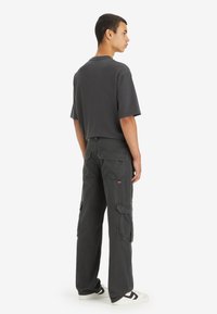 Graues Baumwoll-T-Shirt mit lockerer Passform, kombiniert mit dunkelgrauen Cargo-Hosen, die mehrere Taschen und ein kleines Markenlogo aufweisen.