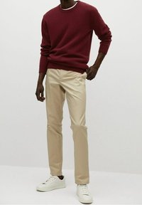 Maglione bordeaux a maglia, pantaloni beige e sneakers bianche. Il maglione ha un colletto rotondo e polsini a coste, i pantaloni sono lisci con una vestibilità dritta.