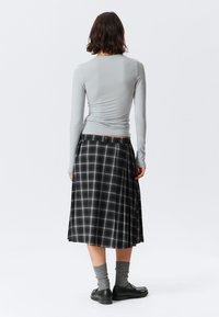 Lichtgrijze lange mouwen top met een getailleerd ontwerp; zwarte geruite midi rok met plooien; grijze kniekousen en zwarte schoenen. Eenvoudige en klassieke look.