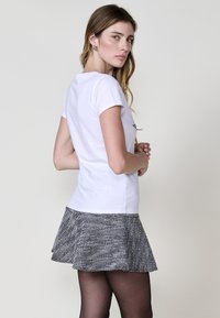 Camiseta blanca de manga corta combinada con una falda acampanada en blanco y negro texturizada. La falda presenta un sutil patrón a cuadros y llega hasta medio muslo.
