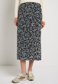 Marineblaue lange Rock mit einem grauen Blumenmuster. Aus weichem Stoff gefertigt, reicht er bis zur Mitte der Wade. Kombiniert mit beigen und braunen Sneakers.