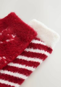 Piros-fehér csíkos zokni, bolyhos textúrával, egyszínű piros felső résszel és fehér alsó résszel. Mintás és puha anyagból készült.