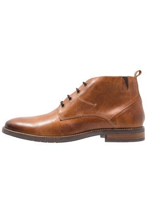 Bottine en cuir marron avec laçage sur le devant, talon à languette, et semelle en bois empilée basse sur fond blanc.