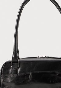 Bolso de mano de cuero negro con textura suave, doble asa, herrajes de plata y cierre con cremallera en la parte superior. Cuenta con un bolsillo frontal.