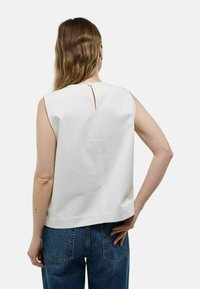 Top blanc sans manches avec un détail en clé à l'arrière, fabriqué dans un tissu lisse ; porté avec un jean bleu taille haute.