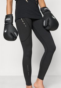 Czarne legginsy o smukłym fasonie i gładkiej fakturze, z jasnobeżowymi akcentami i nadrukowanym napisem na dolnej części nogawki.