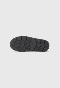 Suela de zapato de goma negra con un patrón de banda de rodadura en zigzag, que presenta un logo circular en el centro y bordes lisos para mejorar la tracción y la estabilidad.