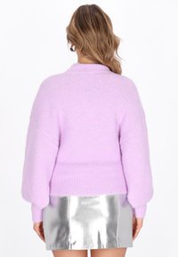 Pull oversized lilas avec ourlet côtelé et manches ballon, associé à une mini-jupe argentée brillante. Texture douce et coupe décontractée.