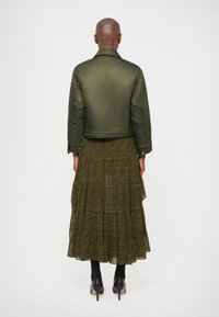 Oliivroheline puffjakker lühikese disainiga, koos musta ja kollase mustriga midi seelikuga, mis sisaldab volange ja läbipaistvaid kihte.