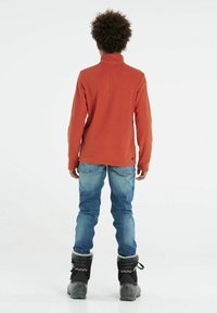 Pullover rosso in fleece con colletto alto, jeans in denim blu e stivali invernali neri con bordi in pelliccia sintetica e suola grigia.
