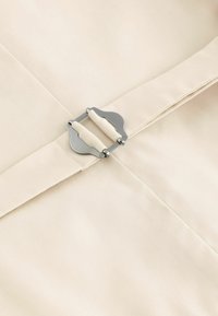 Beige fabric features a metal clasp with a curved design and two fabric straps, showcasing a smooth texture and clean lines.