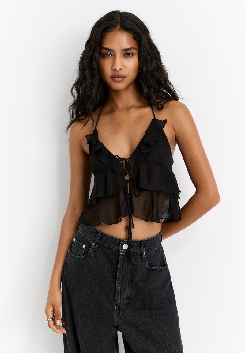 Black chiffon crop top with ruffled layers and adjustable tie closure. Paired with high-waisted black denim jeans.