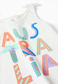 Canotta bianca con lettering colorato che scrive "AUSTRALIA." I design includono palme e motivi astratti in rosa, turchese e viola.