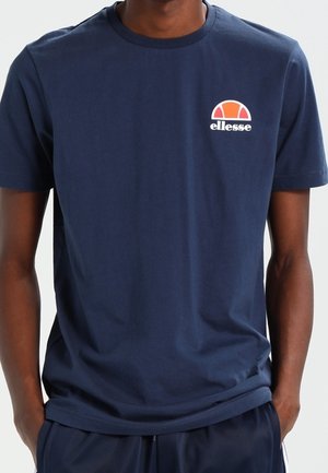 T-shirt en coton bleu marine avec un col rond, des manches courtes et un petit logo blanc et orange sur la poitrine. Texture lisse.