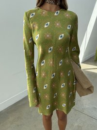 Πράσινο μακρυμάνικο φόρεμα με σχέδιο ματιού και λουλουδιών, υφασμάτινη υφή, μεσαίο μήκος, συνοδευόμενο από μπεζ τσάντα χειρός.