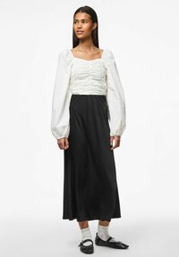 Hvid bluse med pufærmer og indsamlet tekstur, parret med en lang sort nederdel og sorte flade sko. Simpelt, elegant design med kontrasterende farver.