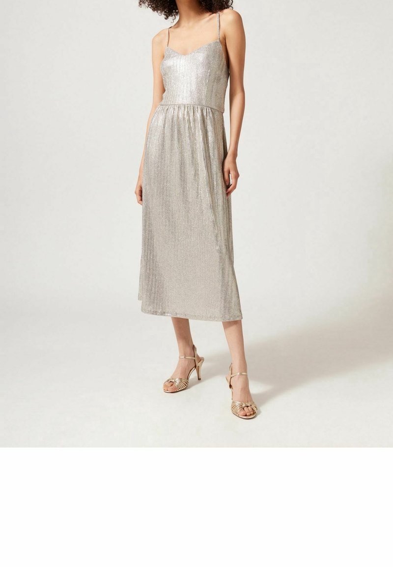 Silverfärgad ärmlös klänning med figurnära liv, plisserad kjol och tunna axelband, i kombination med metalliska högklackade sandaler med remmar.