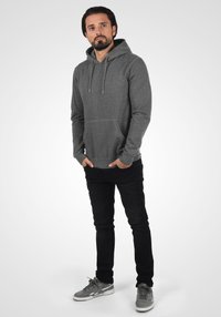 Sweat-shirt à capuche gris avec poche avant, associé à un jean noir et des baskets grises. Doté de cordons de serrage et de poignets ribbed.
