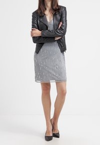 Hopeapintaiset paljetti mekko, jossa on pystysuorat helmiäismallit, on täydentänyt musta nahkainen bikkeritakki. Asusteena mustat teräväkärkiset korkokengät.