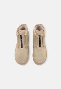 Stivali ankle in suede beige con cerniera davanti, punta arrotondata, fodera morbida e dettagli cuciti lungo la suola.
