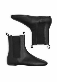 Botas de cuero negro hasta el tobillo con puntera puntiaguda, paneles elásticos en los laterales y lengüetas para facilitar el calzado. Silueta delgada y elegante. Textura suave.
