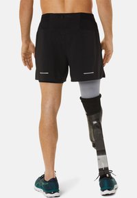 Schwarze Sportshorts mit reflektierenden Akzenten, kombiniert mit einem blauen und schwarzen Laufschuh. Ein Prothesenbein mit Karbonfaser-Optik ist zu sehen.