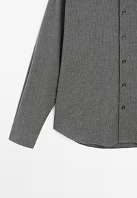 Camicia grigia abbottonata con tessuto strutturato, maniche lunghe, orlo curvo e sette bottoni neri lungo la parte anteriore.