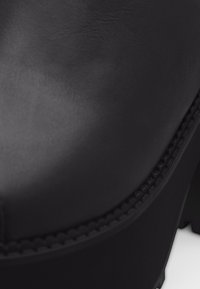 Gros plan sur le bout d'une chaussure en cuir noir avec des coutures détaillées le long du bord.