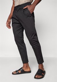 Pantalones negros de corte ajustado con una cinturilla elástica, bolsillos laterales y un fit slim, combinados con sandalias negras texturizadas con recortes.
