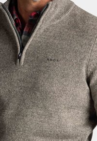 Grijs pullover trui met een kwart-rits kraag, gestructureerde stof en subtiele stikdetails. Heeft een klein logo op de borst.