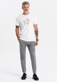 Witte katoenen t-shirt met een palmbom en de print "CALIFORNIA"; gecombineerd met grijze cargobroeken en zwarte sportschoenen.