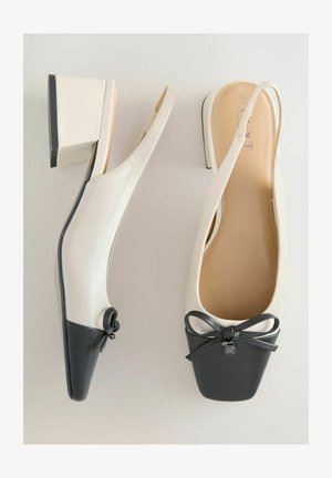 Slingback topánky s blokovým podpätkom z krémovej kože s čiernou špičkou, zdobené dekoratívnou mašľou a malým príveskom na prednej strane.