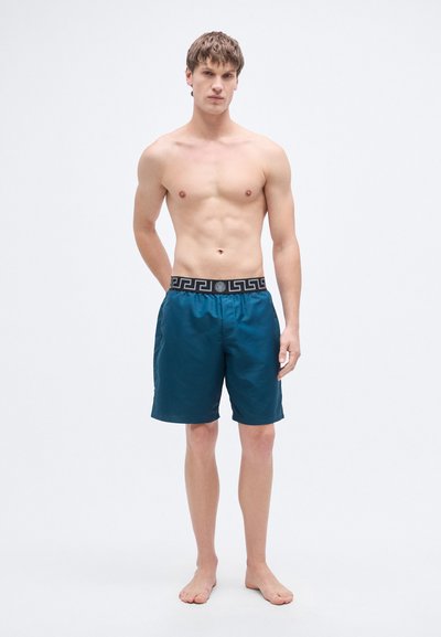 Μαγιό σορτς σε βαθύ τιρκουάζ με ελαστική μέση σε μαύρο με μοτίβο. Ελαφρύ ύφασμα, μήκος μέχρι τα γόνατα και λεία υφή.