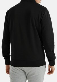 Zwart sweatshirt met een hoge kraag, lange mouwen en geribde manchetten. Glad materiaal en een aansluitend ontwerp, gecombineerd met lichtgrijze broek.